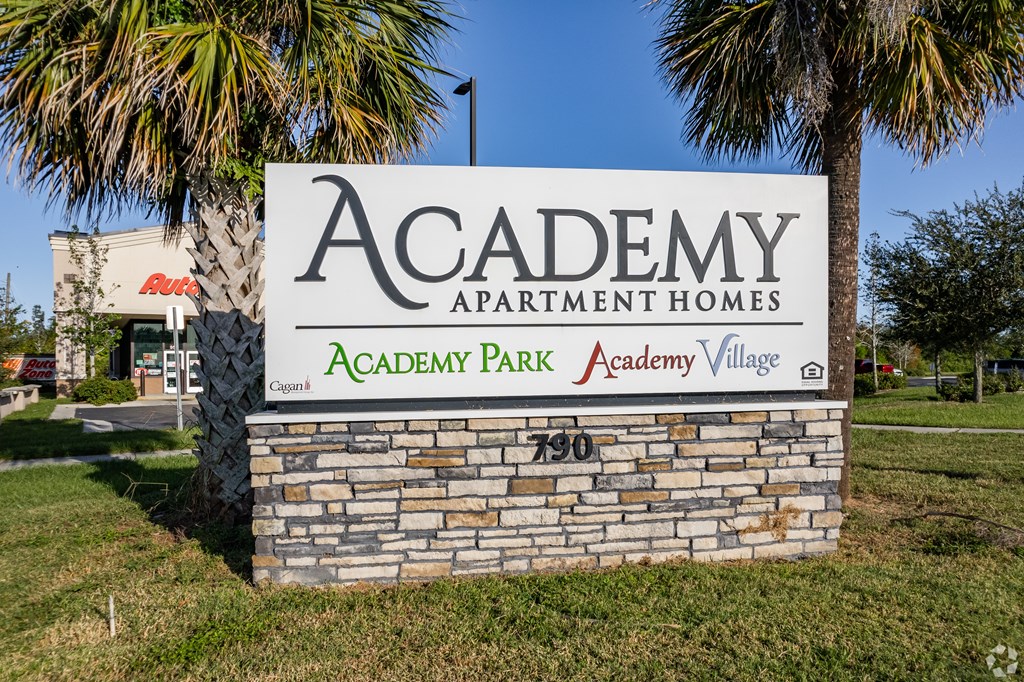 A stone sign for Academy Park Apartment Homes stands in front of a palm tree.