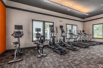 A gym with a variety of cardio equipment including treadmills, stationary bikes, and elliptical machines.