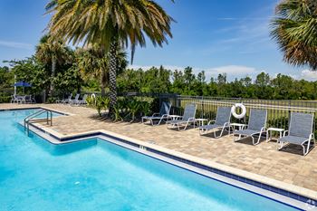 A pool surrounded by palm trees and lounge chairs.