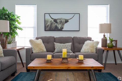 A living room with a grey couch, a wooden coffee table, and a painting of a bull on the wall.