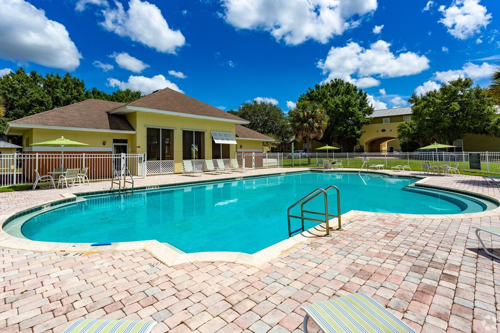 A swimming pool surrounded by a brick patio and a yellow building in the background.