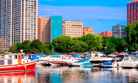 A red boat is docked in a marina with other boats and buildings in the background.