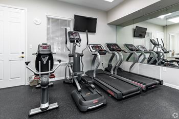A gym with treadmills, elliptical machines, and a television.