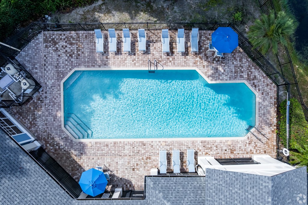 A rectangular pool surrounded by a brick patio and lounge chairs.