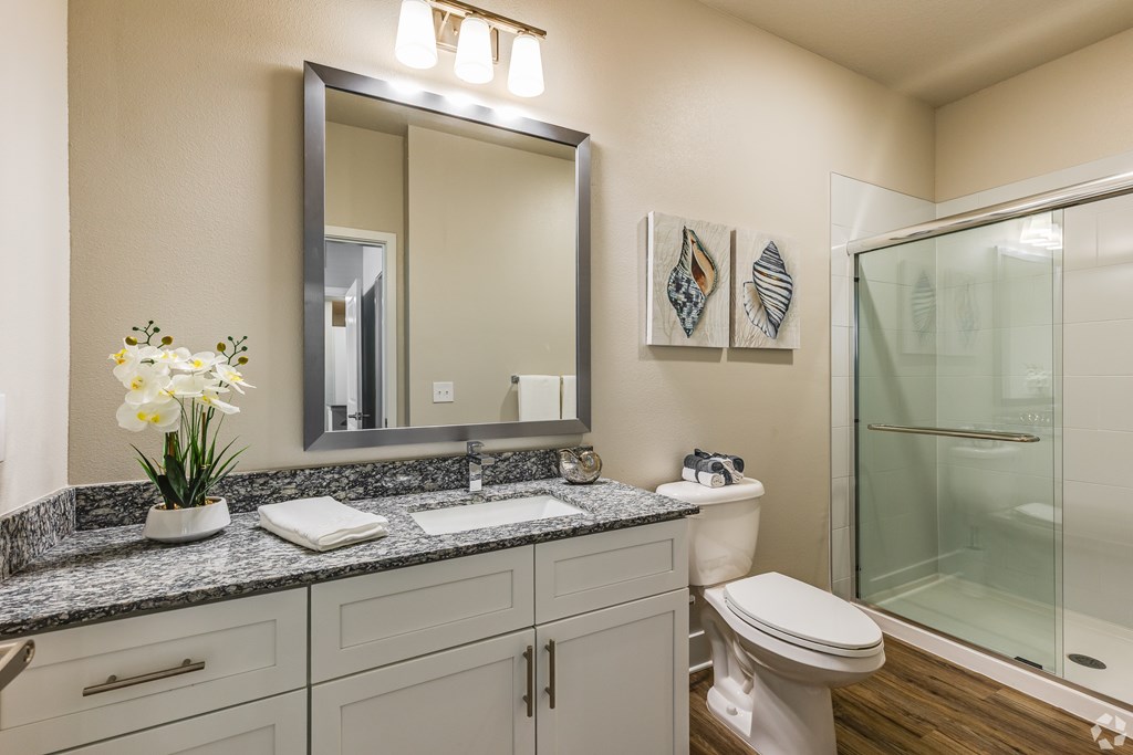 A bathroom with a toilet, sink, mirror, and a vase of flowers.