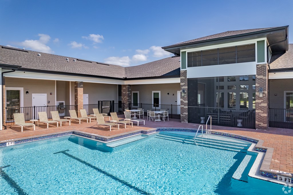 A swimming pool in front of a building with lounge chairs around it.
