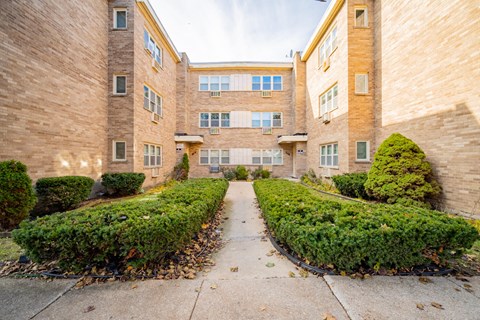 A building with a long hallway and bushes on either side.