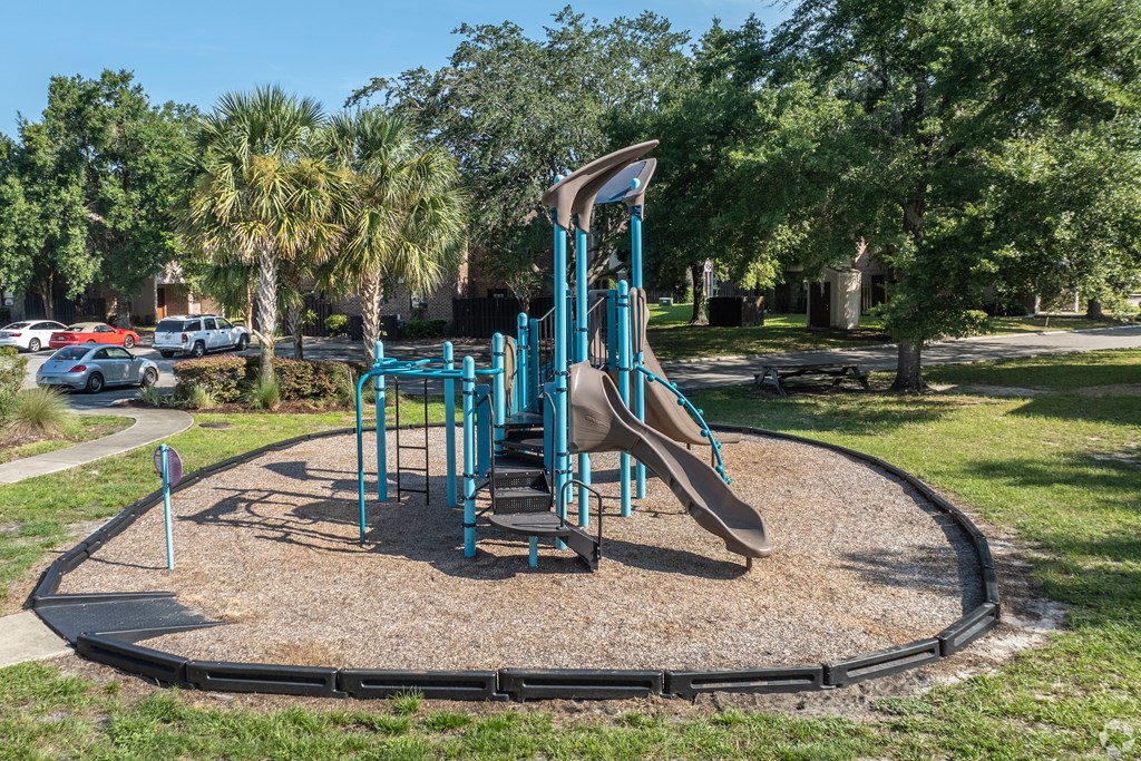 A playground with a blue slide and a brown sandbox.