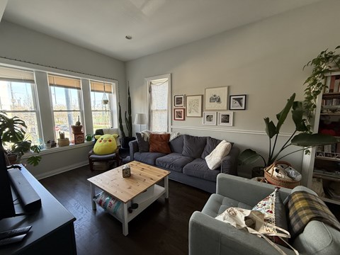 A living room with a grey couch, a wooden coffee table, and a large window.