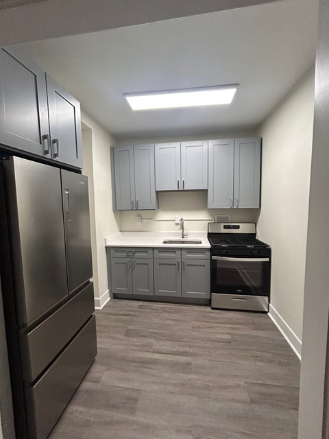 A kitchen with a stainless steel refrigerator and grey cabinets.