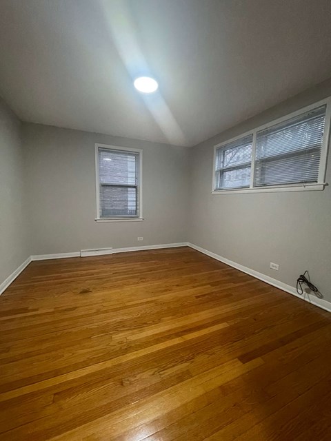 A room with wooden flooring and two windows.