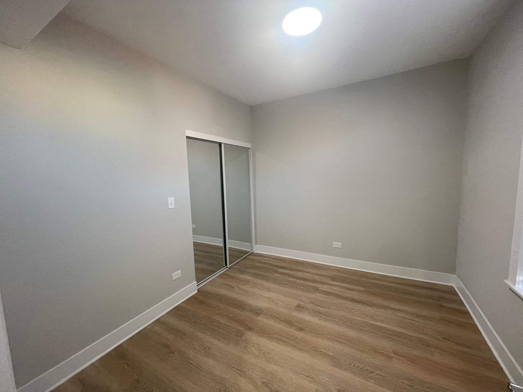 a bedroom with hardwood flooring and a mirrored closet