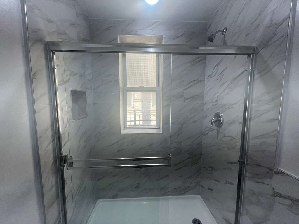 a large shower with a glass door in a white marble bathroom