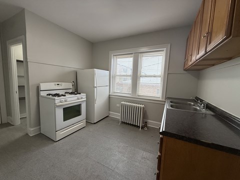 A kitchen with a white stove and refrigerator, a window with blinds, and a sink with a black countertop.
