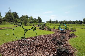 A metal sculpture of interconnected circles and gears sits in a mulched garden bed.