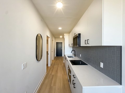 A long, narrow kitchen with white cabinets and a black backsplash.