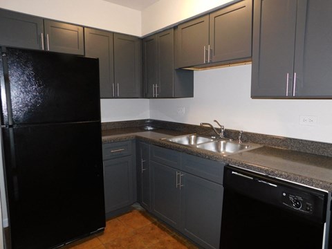 A black refrigerator stands in a kitchen with grey cabinets.