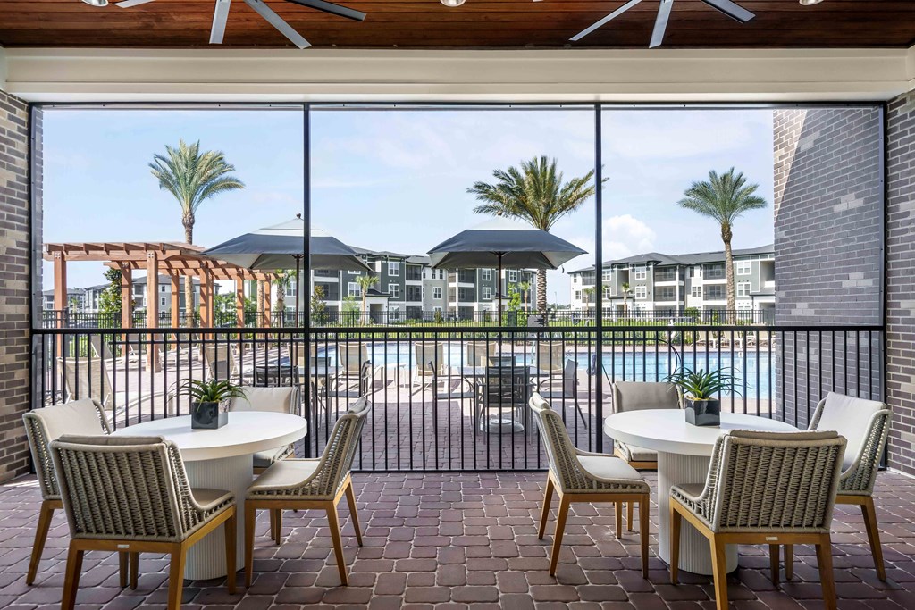A patio with a table and chairs overlooking a pool and buildings.