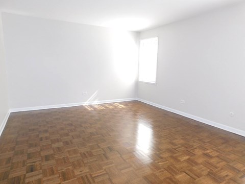 A room with wooden flooring and a window letting in sunlight.