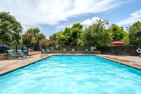 A large blue swimming pool surrounded by trees and lounge chairs.