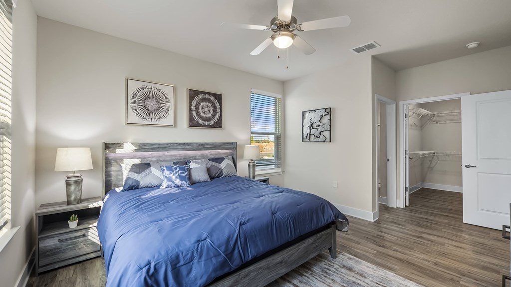 A bedroom with a blue bedspread and a ceiling fan.