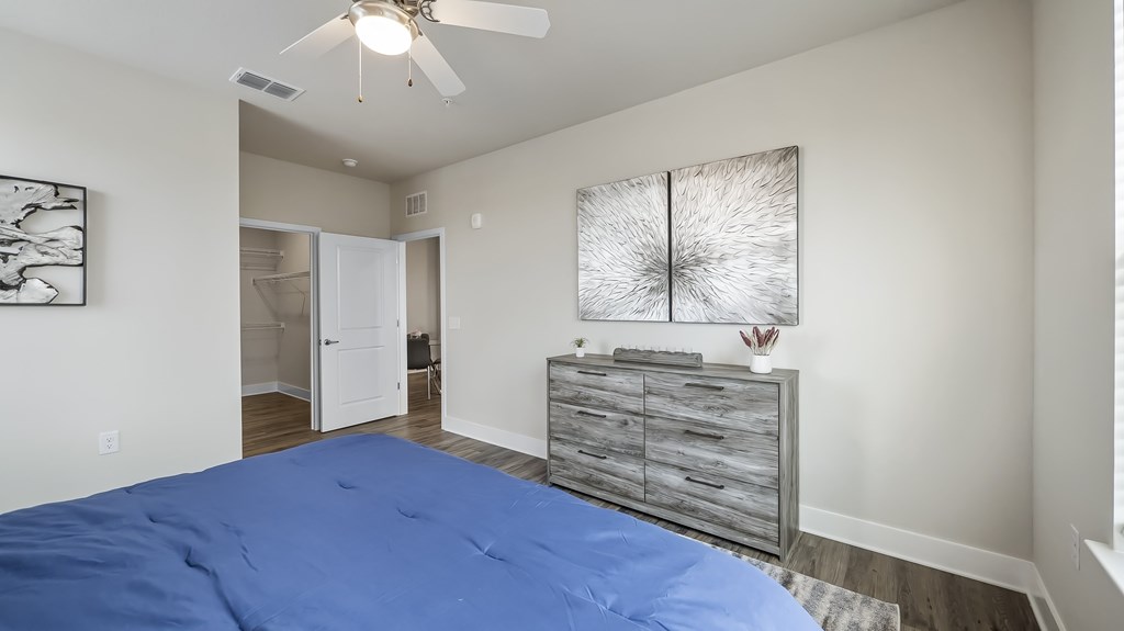 A bedroom with a blue bedspread and a ceiling fan.