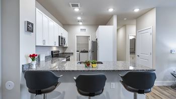 A kitchen with a granite countertop and black chairs.
