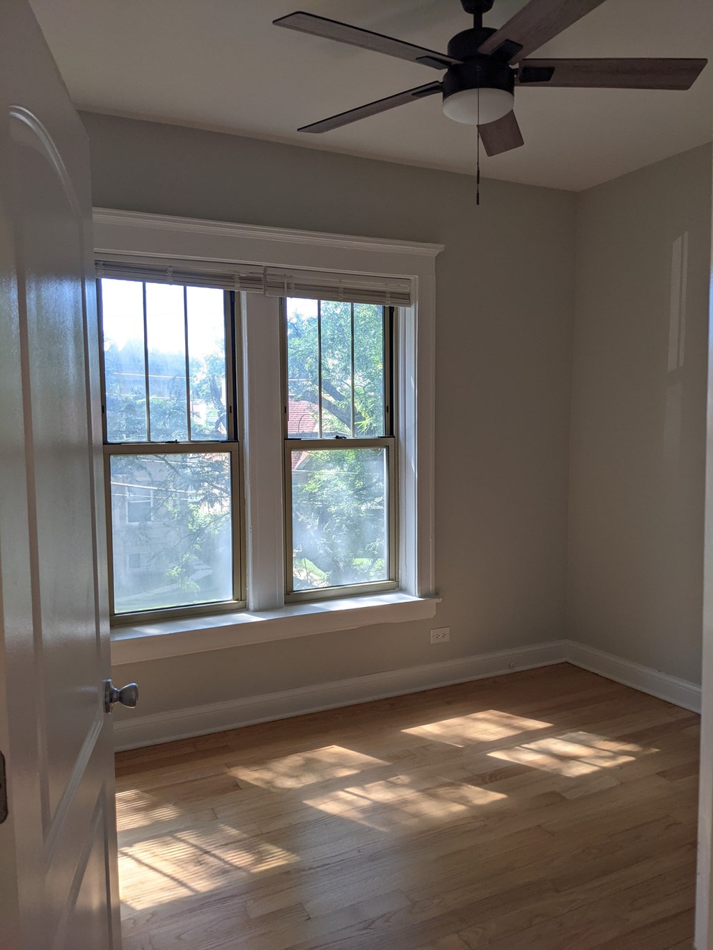 A room with a ceiling fan and a window with sunlight coming through.