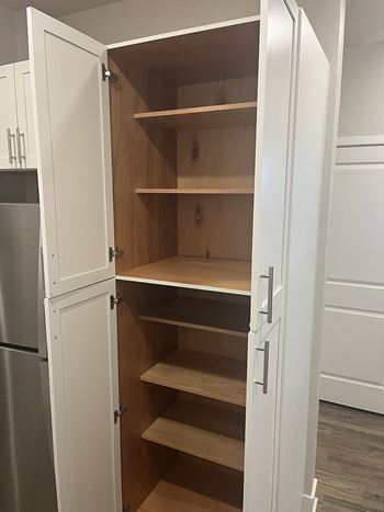 A white kitchen cabinet with a door open revealing shelves.