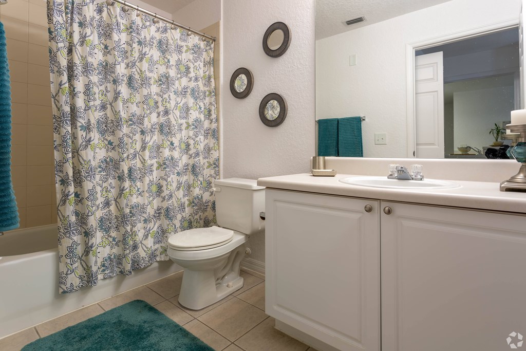 A white bathroom with a floral shower curtain and a green rug.