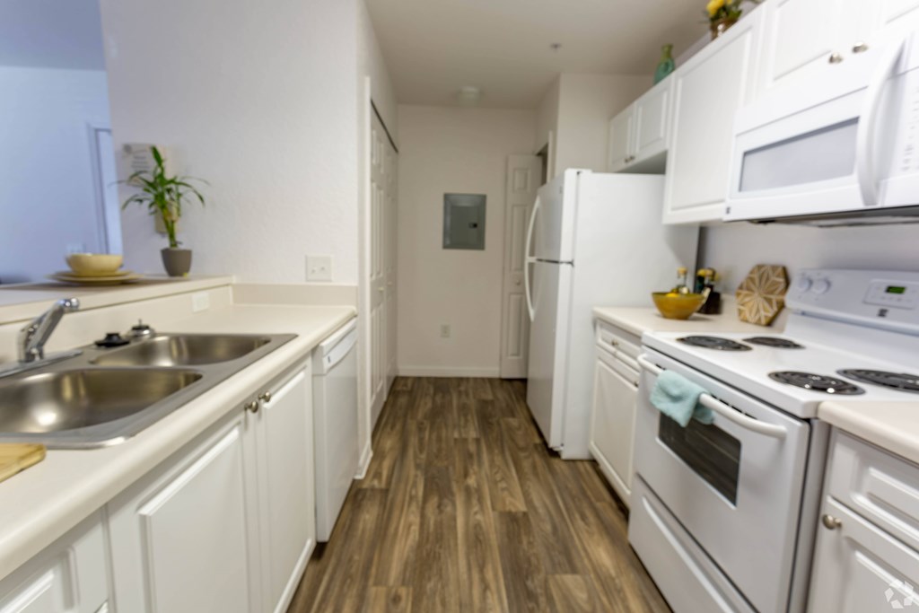 A kitchen with white appliances and wooden floors.
