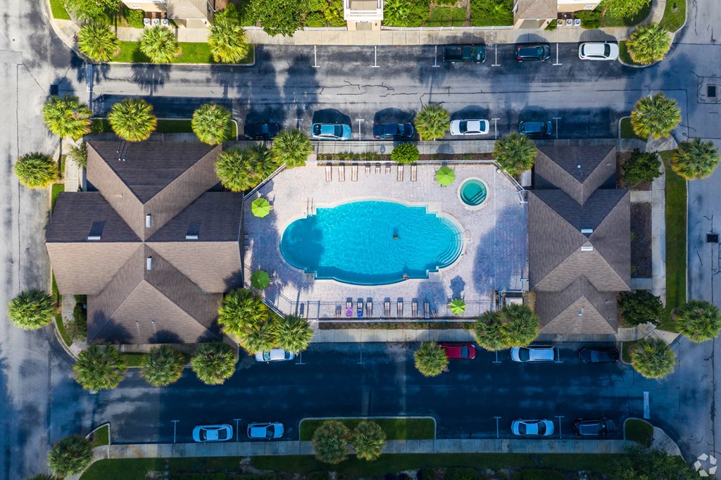 A bird's eye view of a residential area with houses, a swimming pool, and a parking lot.