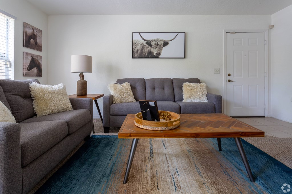 A living room with a grey couch, a wooden coffee table, and a painting of a cow on the wall.