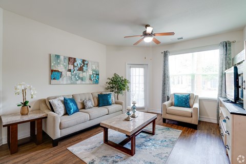 A living room with a beige couch, a coffee table, and a ceiling fan.