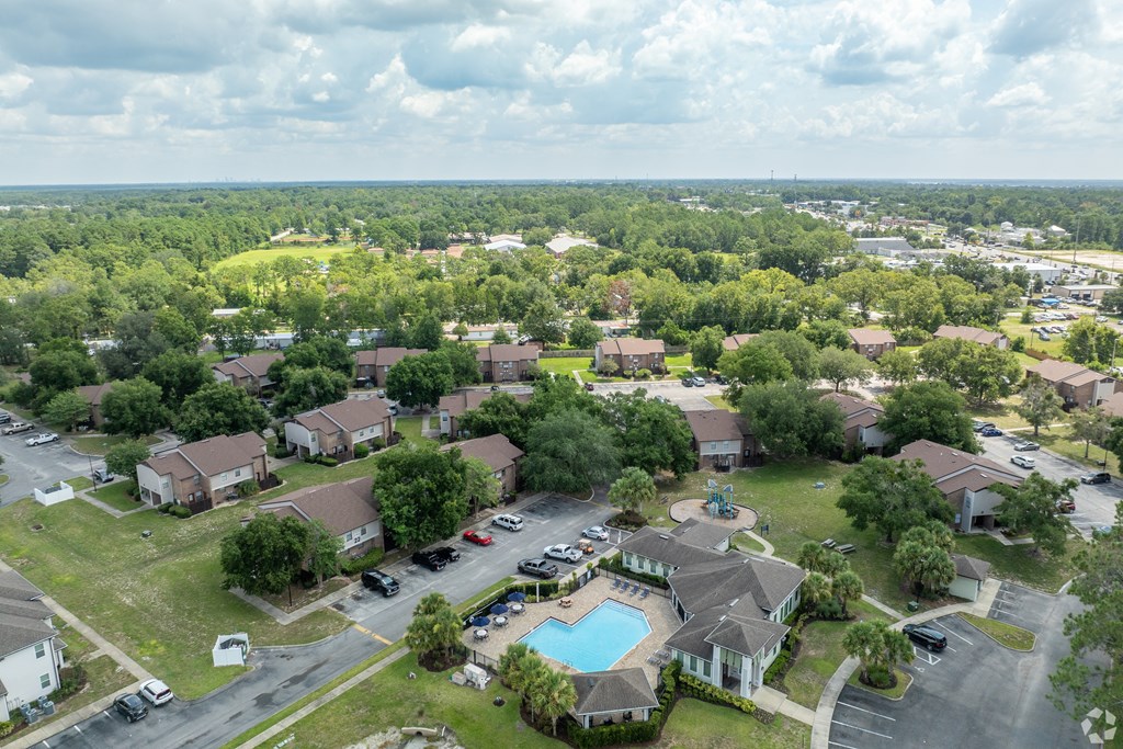 A bird's eye view of a residential area with houses, a swimming pool, and a parking lot.