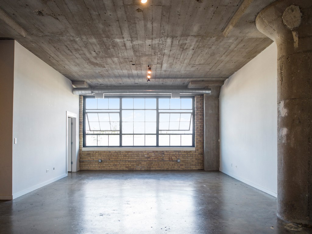 an empty room with a window and concrete floors and a brick wall