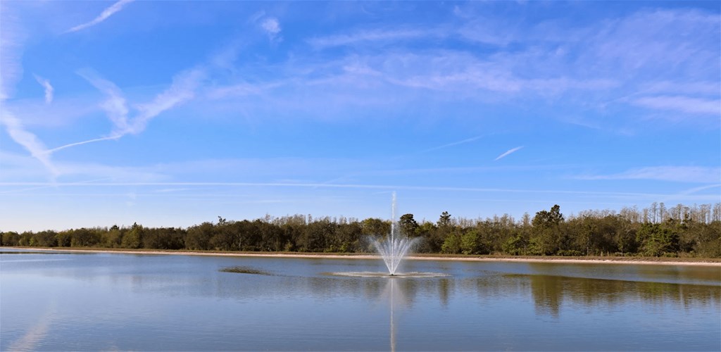 A fountain in the middle of a lake with trees in the background.