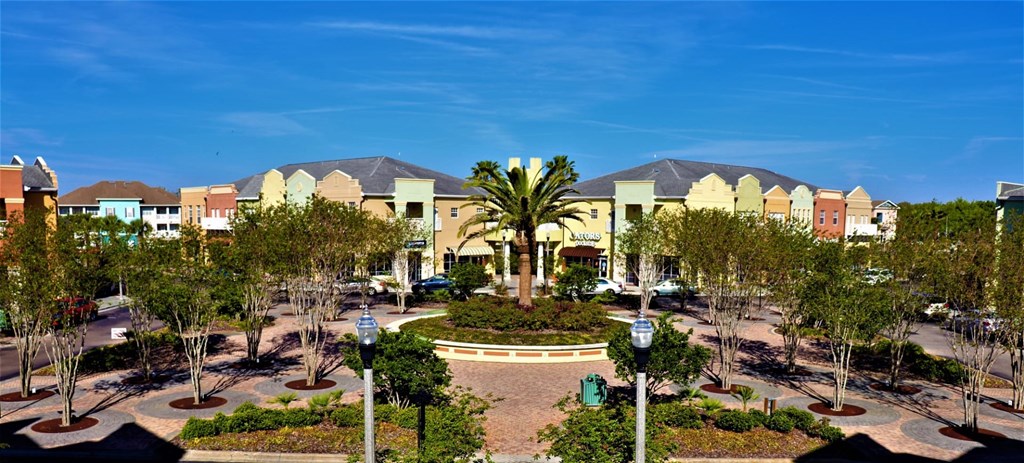 A large building with a yellowish hue is surrounded by trees and a fountain in the middle of a plaza.