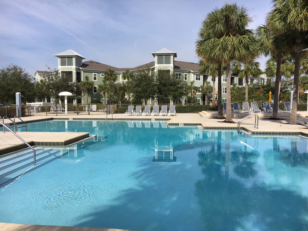 A large swimming pool in front of a building with palm trees.