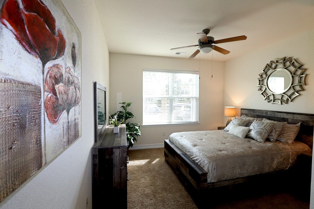 A bedroom with a bed, a ceiling fan, and a painting of a flower on the wall.