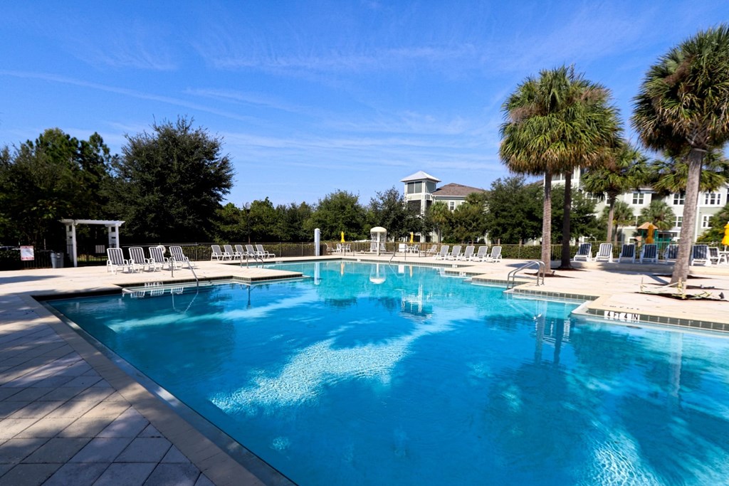 A large swimming pool with a white fence and chairs around it.