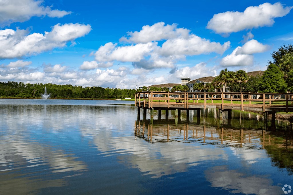 A wooden pier extends into a calm body of water under a blue sky with scattered clouds.