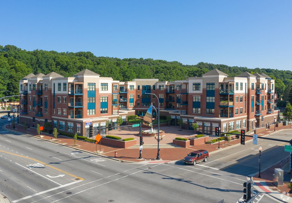A street view of a town with apartment buildings and a car driving on the road.