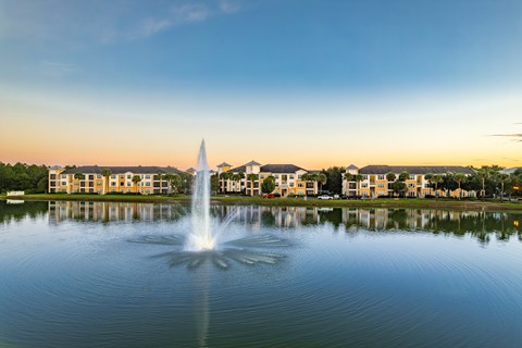 A fountain in the middle of a lake with buildings in the background.