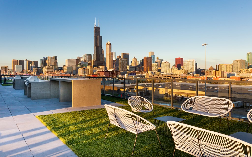 Three white chairs are on a patio overlooking a city skyline.