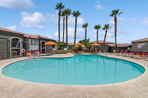 2-Bedroom Apartments in North Las Vegas, NV - Loma Vista - Resort-Style Swimming Pool With Palm Trees, Orange Umbrellas, Lounge Chairs, And Fenced Sundeck Surrounded By Community Buildings.