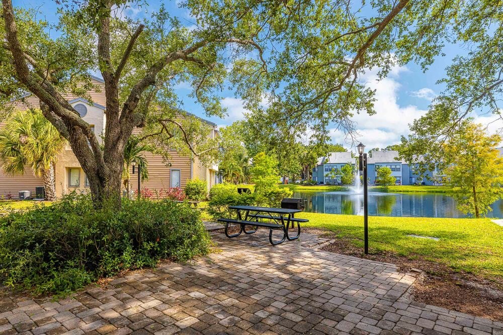 Picnic table near lake surrounded by greenery at Huntington Place Apartments in Sarasota, Florida