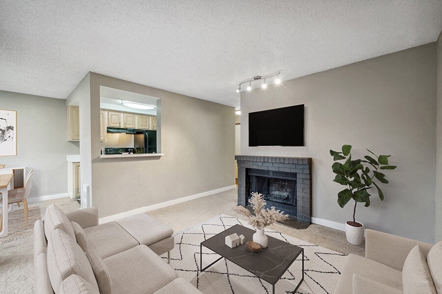 Model Living Room with Carpet, Fireplace and View of Kitchen at Grammercy Apartments located in Renton, WA.
