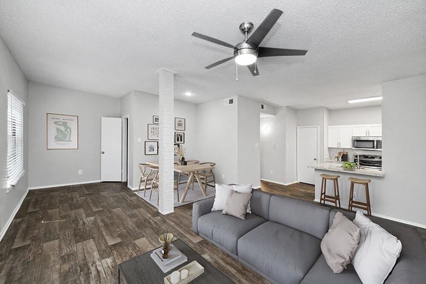 Model Living Room and Dining Room Area with Wood-Style Flooring and View of Kitchen at Heatherstone Apartments in Dallas, TX.
