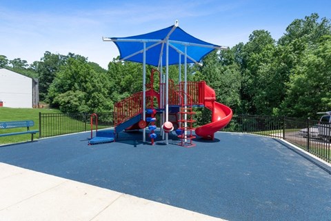 Woodbridge, VA, Apartments Near Potomac Mills Mall - Brightwood Forest - A Playground With Red Slides, Climbing Structures, And A Blue Shade Canopy On Rubber Surfacing.